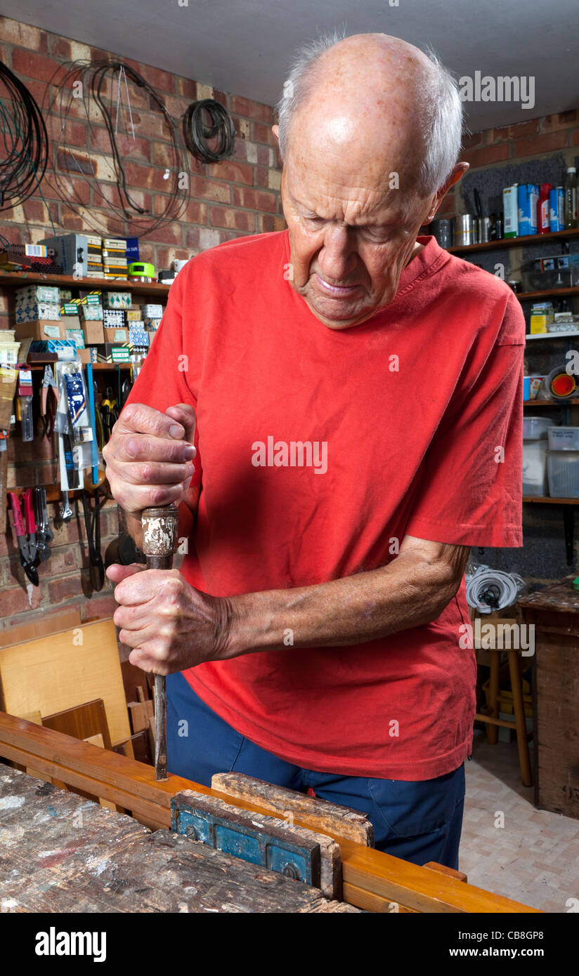 Elderly gentleman in his workshop using a screwdriver to remove an old screw from  a piece of wood Stock Photo