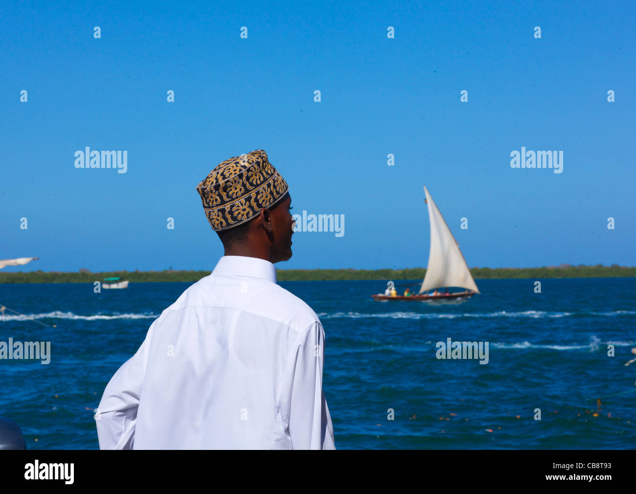 Man With Kofia, Looking Towards The Sea, Dhow Passing In The Channel, Lamu, Kenya Stock Photo