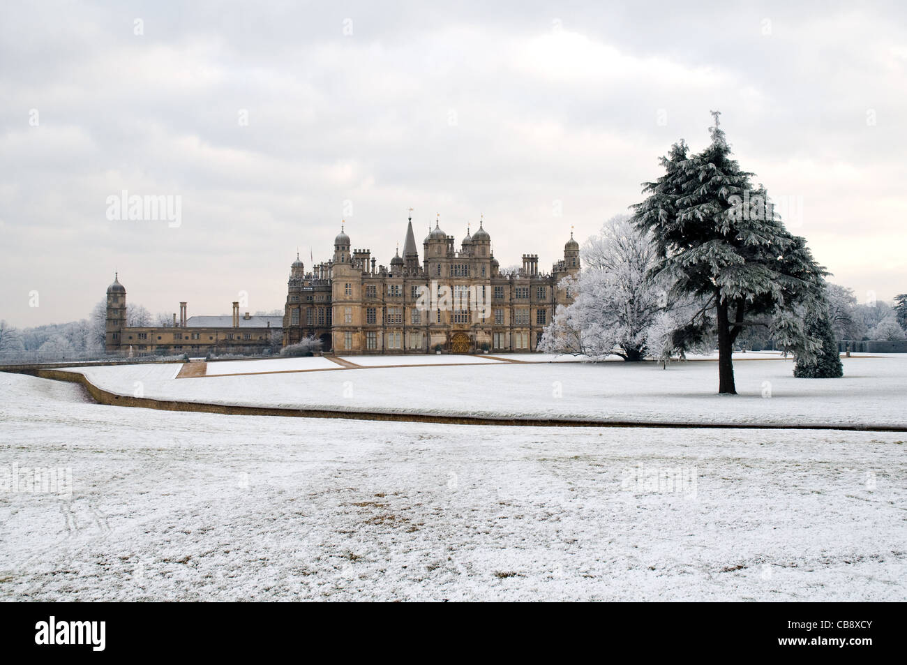 Burghley House in the snow with trees in the foreground. Stock Photo