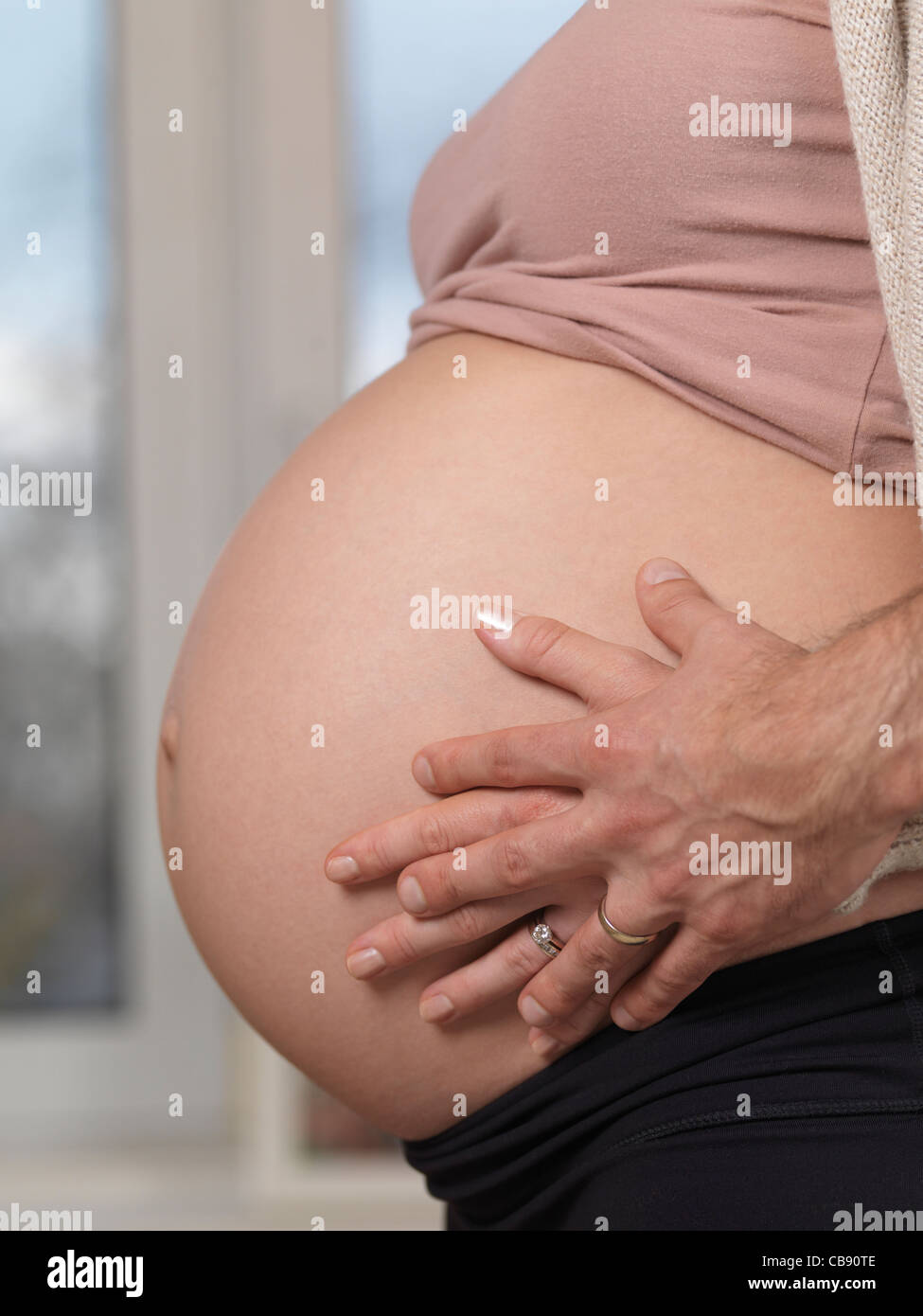 Closeup of a husband holding his hands around his pregnant wife's belly Stock Photo