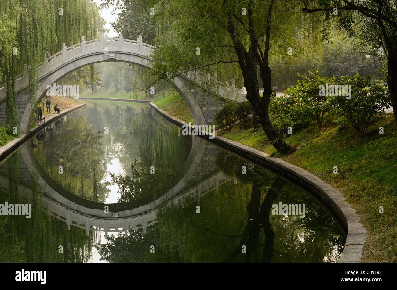 Men fishing on peaceful Changhe river with stone bridge in Zizhuyuan Purple Bamboo Park Beijing Peoples Republic of China Stock Photo