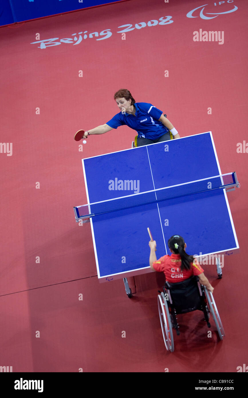 Female wheelchair table tennis player reaches to hit a return during