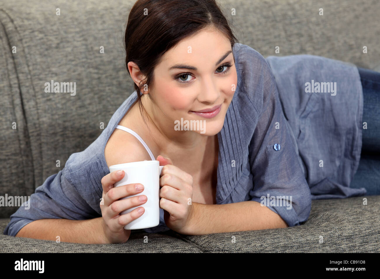 Woman laying on sofa with mug of coffee Stock Photo