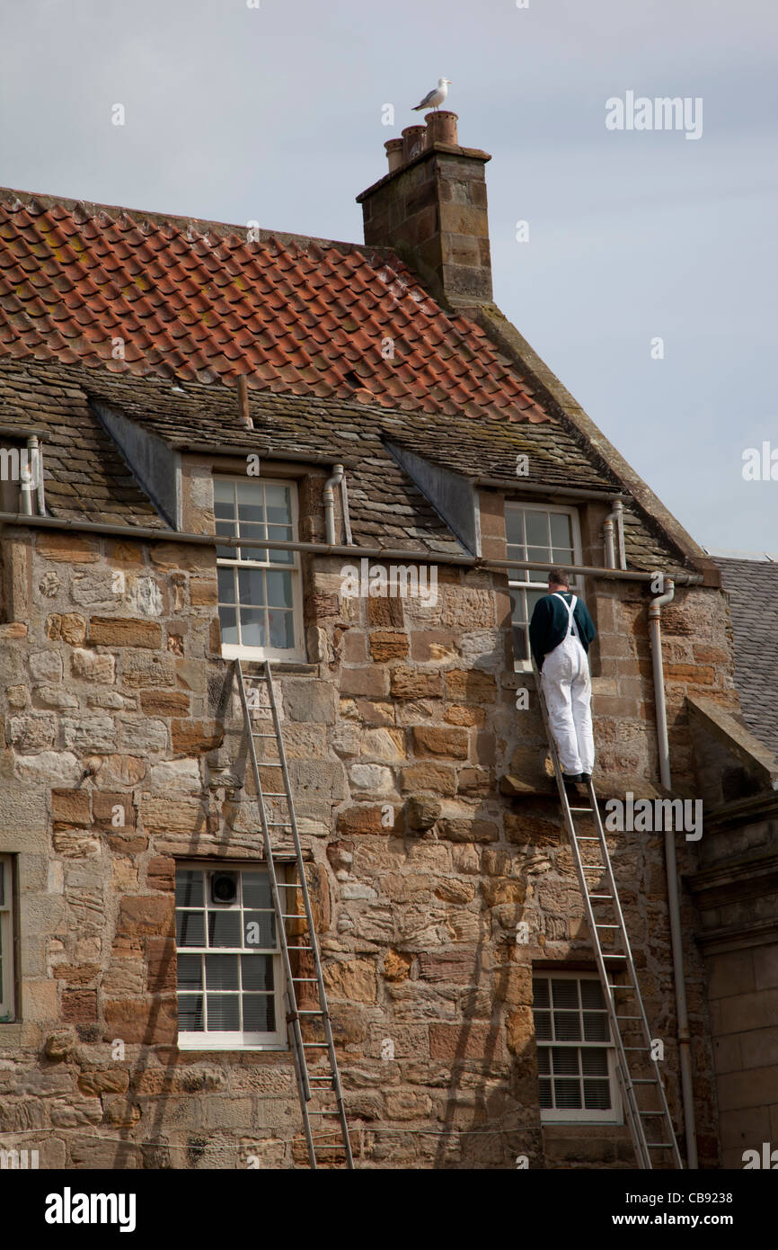 Man in white overalls up a ladder painting a window on an old house in Anstruther, Fife, Scotland Stock Photo