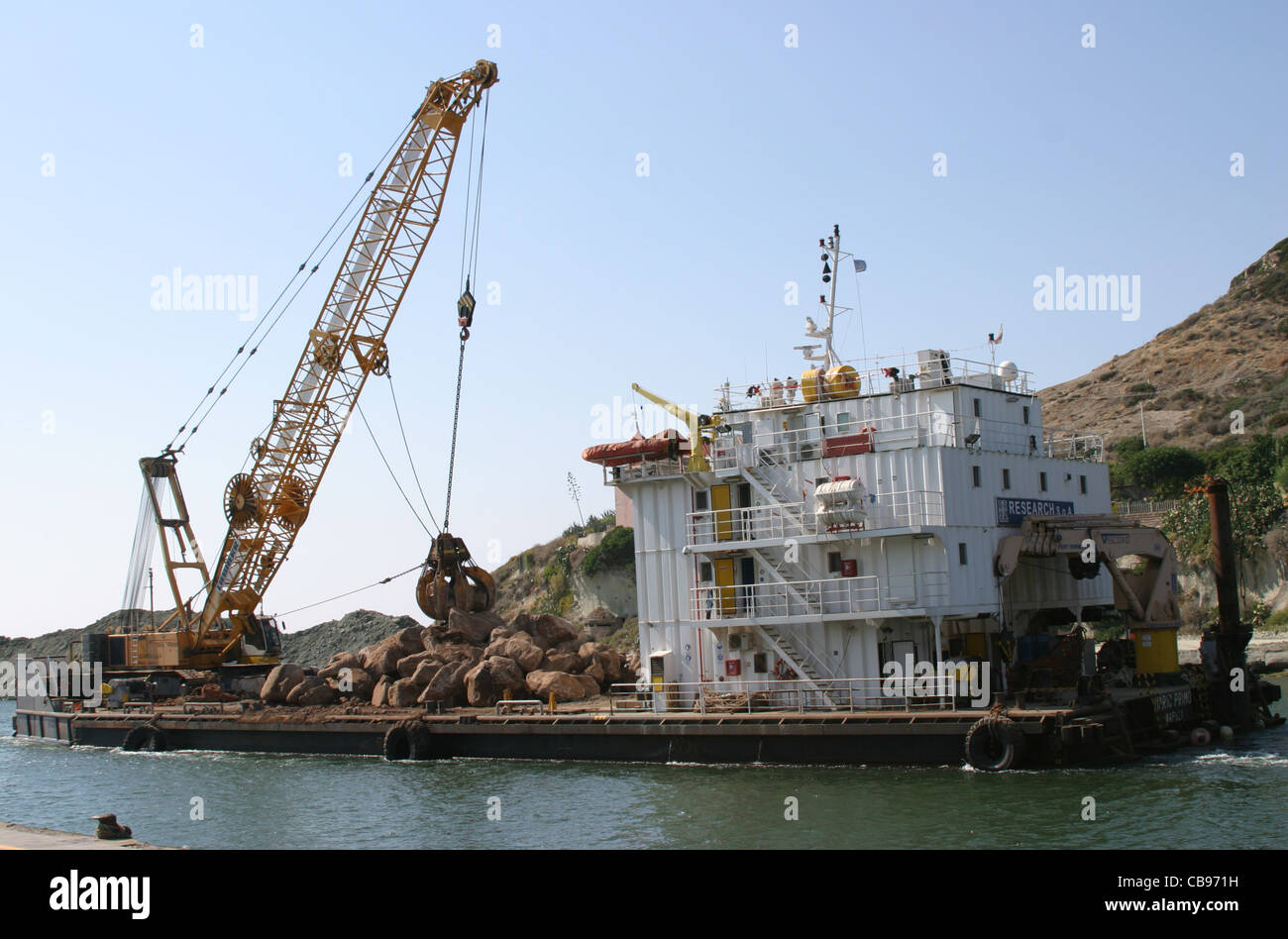 MS Mario Primo lay barge and stone dumping vessel on the construction of harbour wall in Bosa, Sardinia with hydraulic crane Stock Photo