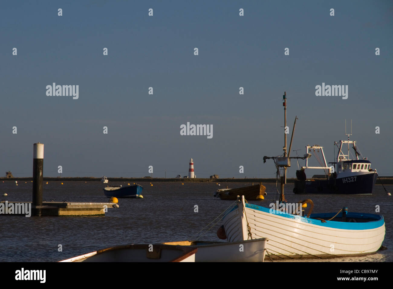 Boats moored at Orford Quay in Suffolk, England, with Orford Ness lighthouse in the far distance Stock Photo