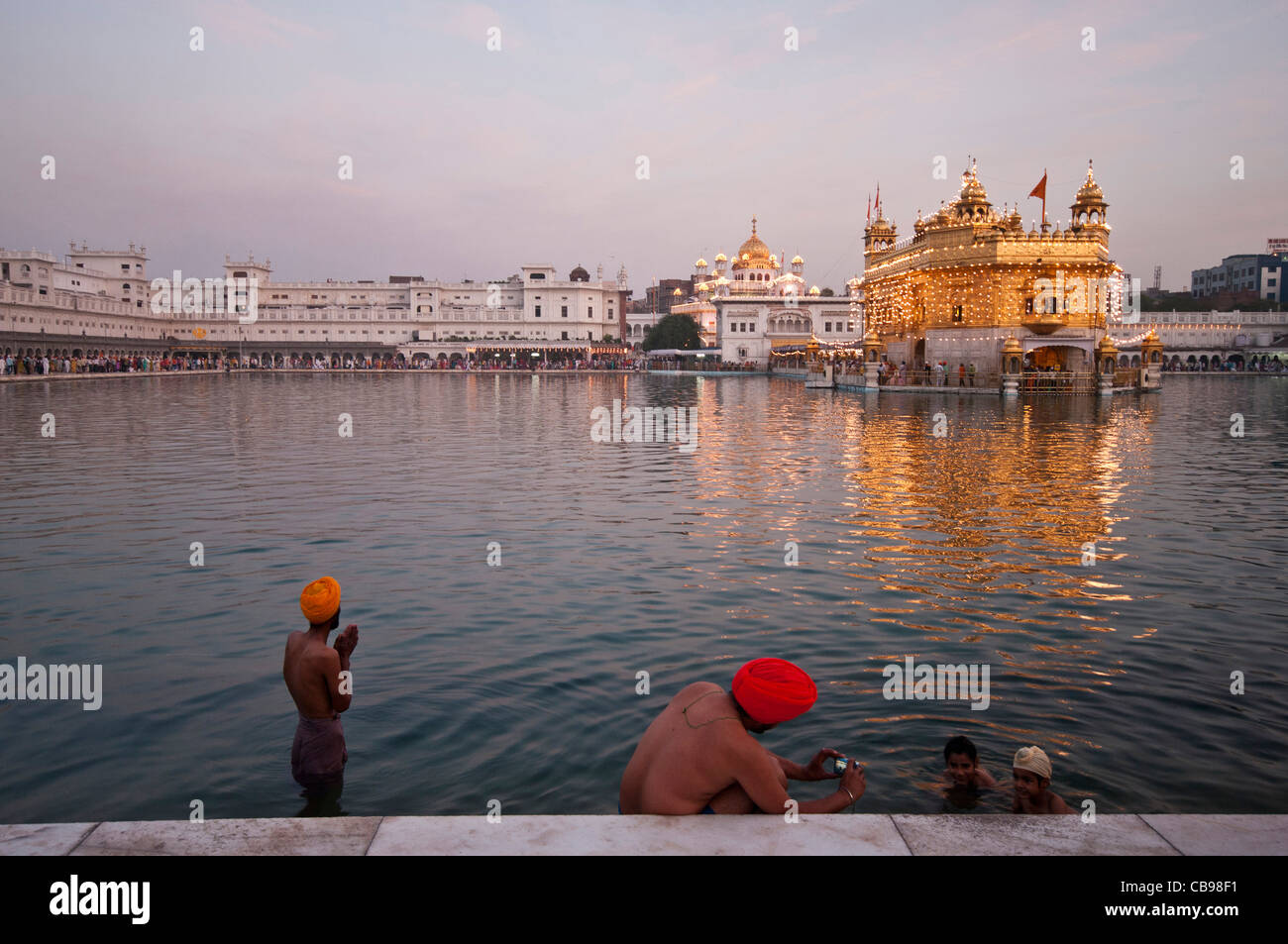 Ritual bathing at Amritsar Golden temple in Punjab, India. A man prays while another takes a photograph of his children. Stock Photo