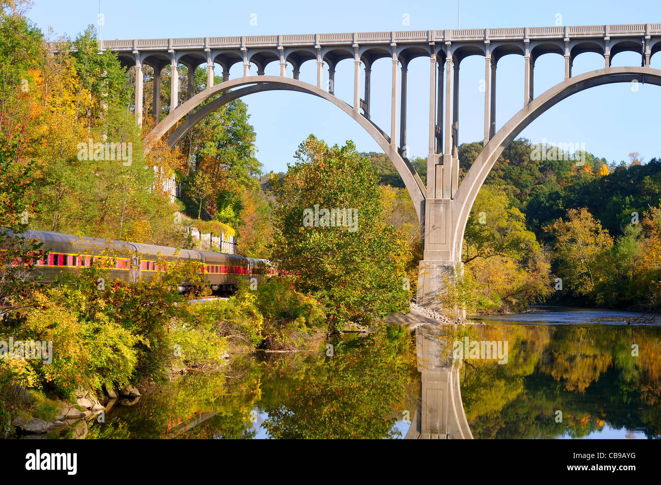 Passenger cars of a train pass under a high bridge in a scenic area Stock Photo