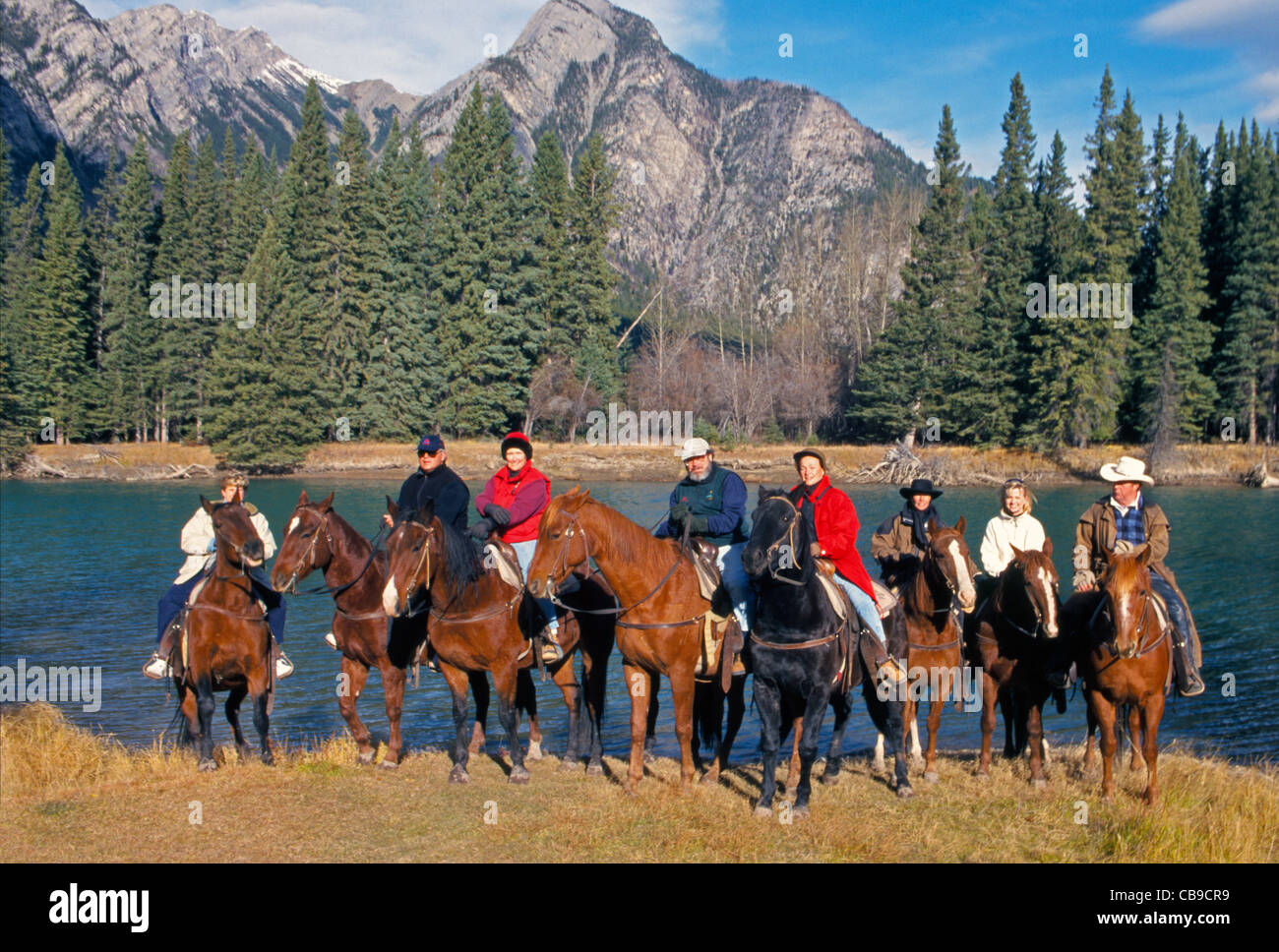 Horseback riders on a vacation trip pause by the Bow River during a trail ride in Banff National Park in the Canadian Rockies in Alberta, Canada. Stock Photo