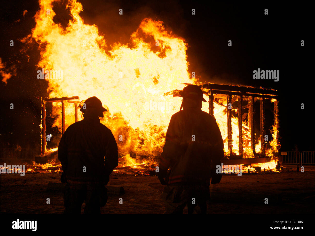 Two firemen watch a house burning out of control. Stock Photo