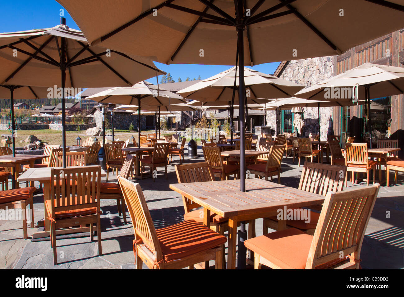 Outdoor patio dining at a mountain resort lodge with umbrellas over wood tables and chairs Stock Photo