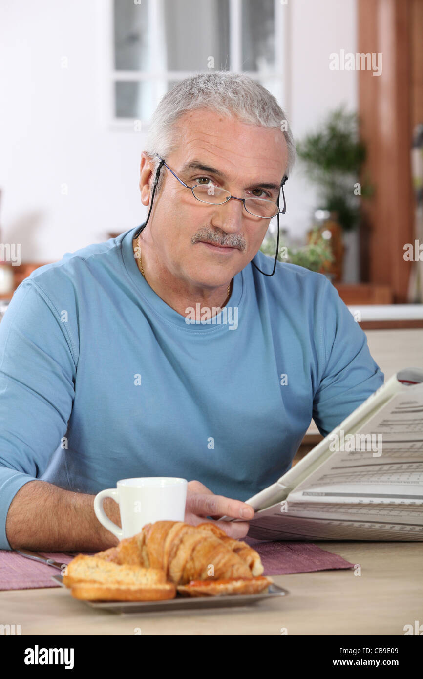 Middleaged man reading newspaper whilst eating breakfast Stock Photo
