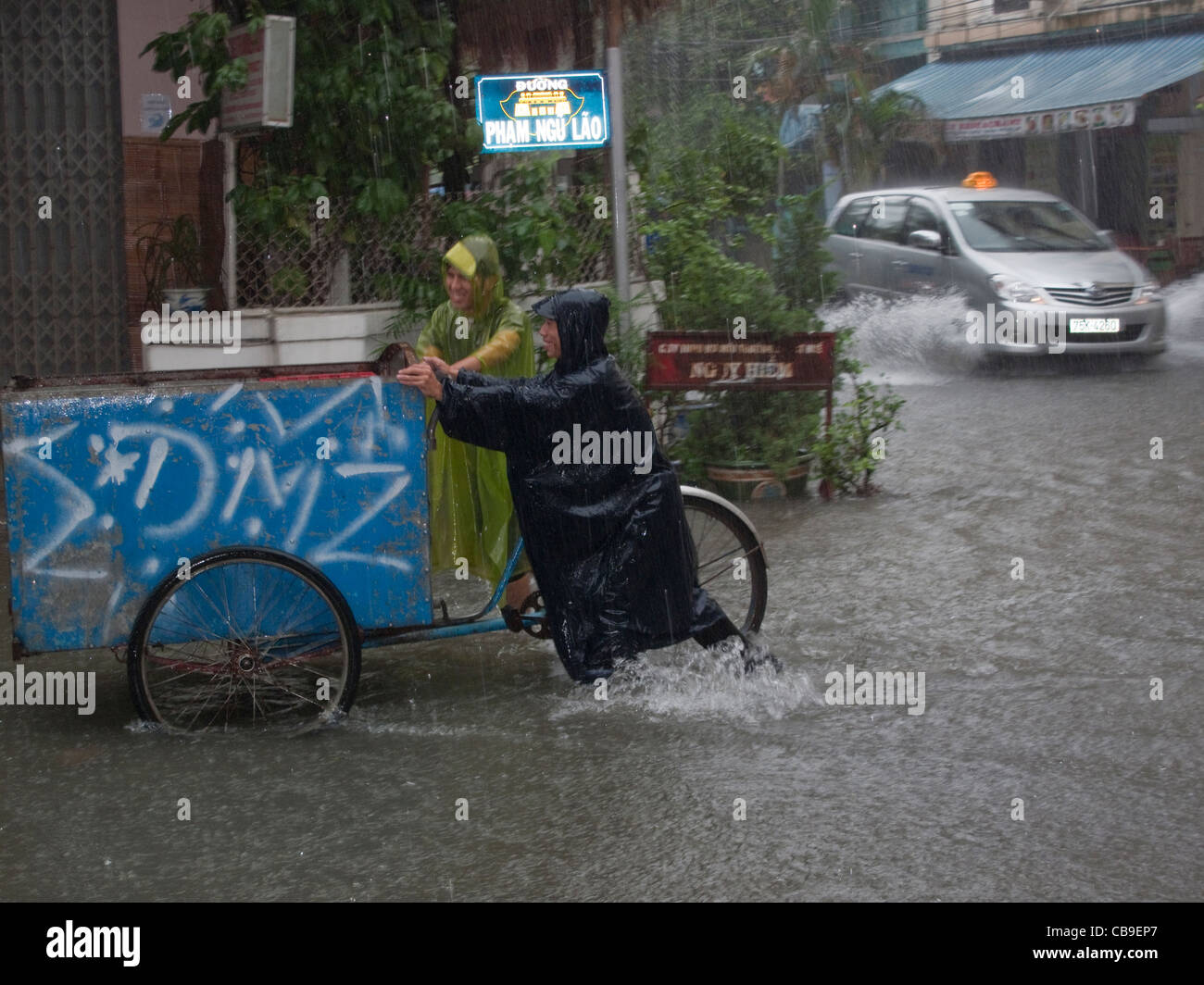Street vendors pushing a tricycle through a flooded street caught in a monsoon rain downpour in Hue, Vietnam Stock Photo