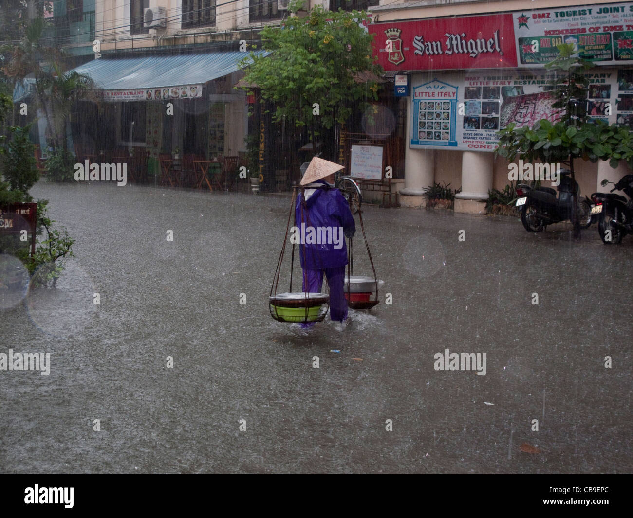 Woman street vendor caught in monsoon rain downpour in a city street in Hue, Vietnam Stock Photo