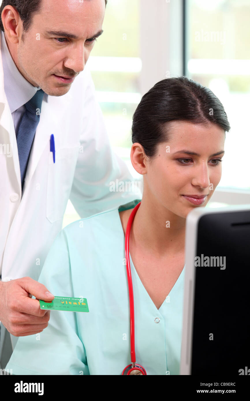 Doctor and nurse looking up a French Carte Vitale on a computer Stock Photo