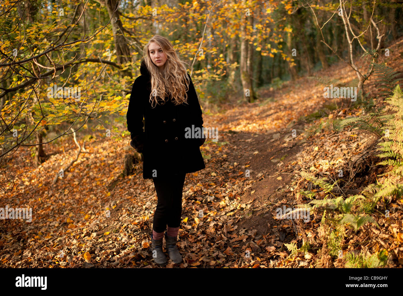 a slim pensive blonde woman girl standing alone in woodland autumn afternoon daytime UK Stock Photo