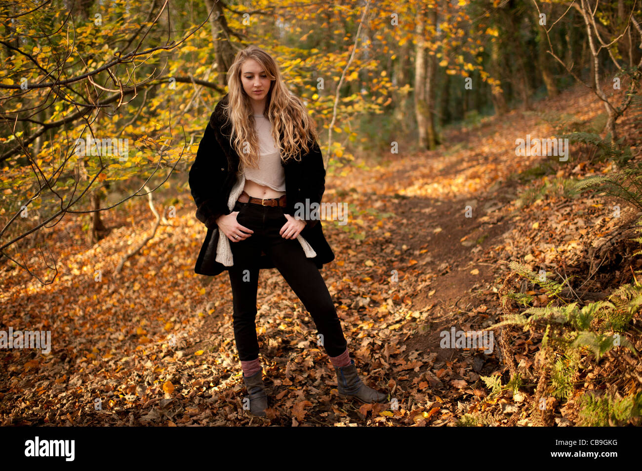 a slim blonde woman girl standing alone in woodland autumn afternoon daytime UK Stock Photo