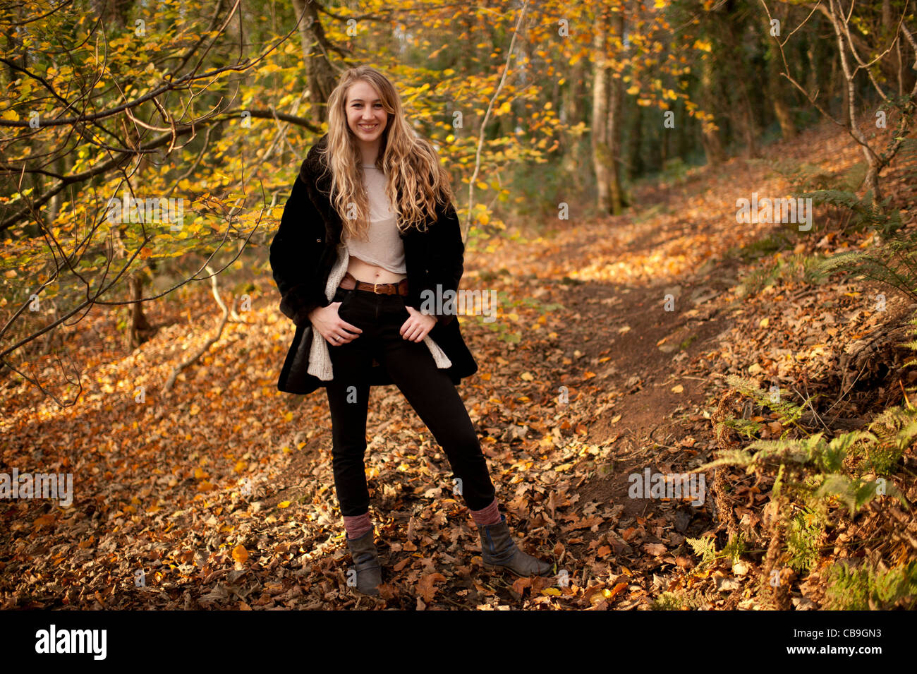 a smiling happy slim blonde woman girl alone in woodland autumn afternoon daytime UK Stock Photo