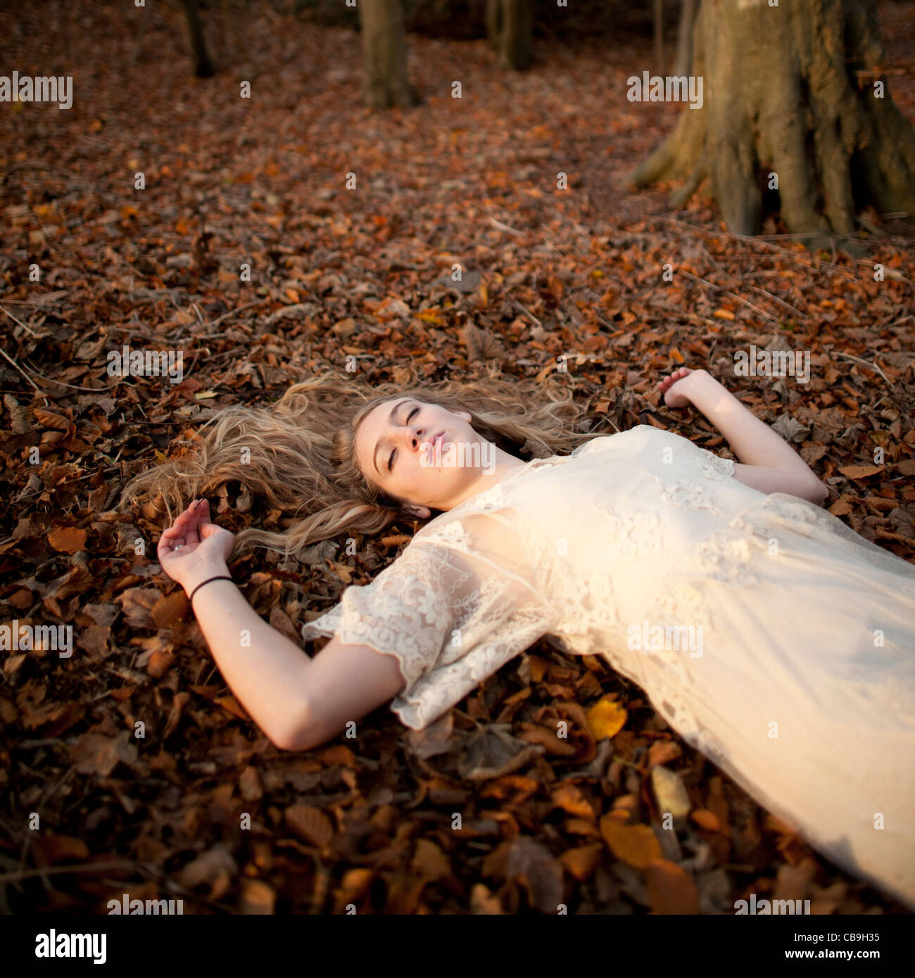 asleep on the ground - a slim blonde woman girl alone in woodland autumn afternoon daytime UK Stock Photo