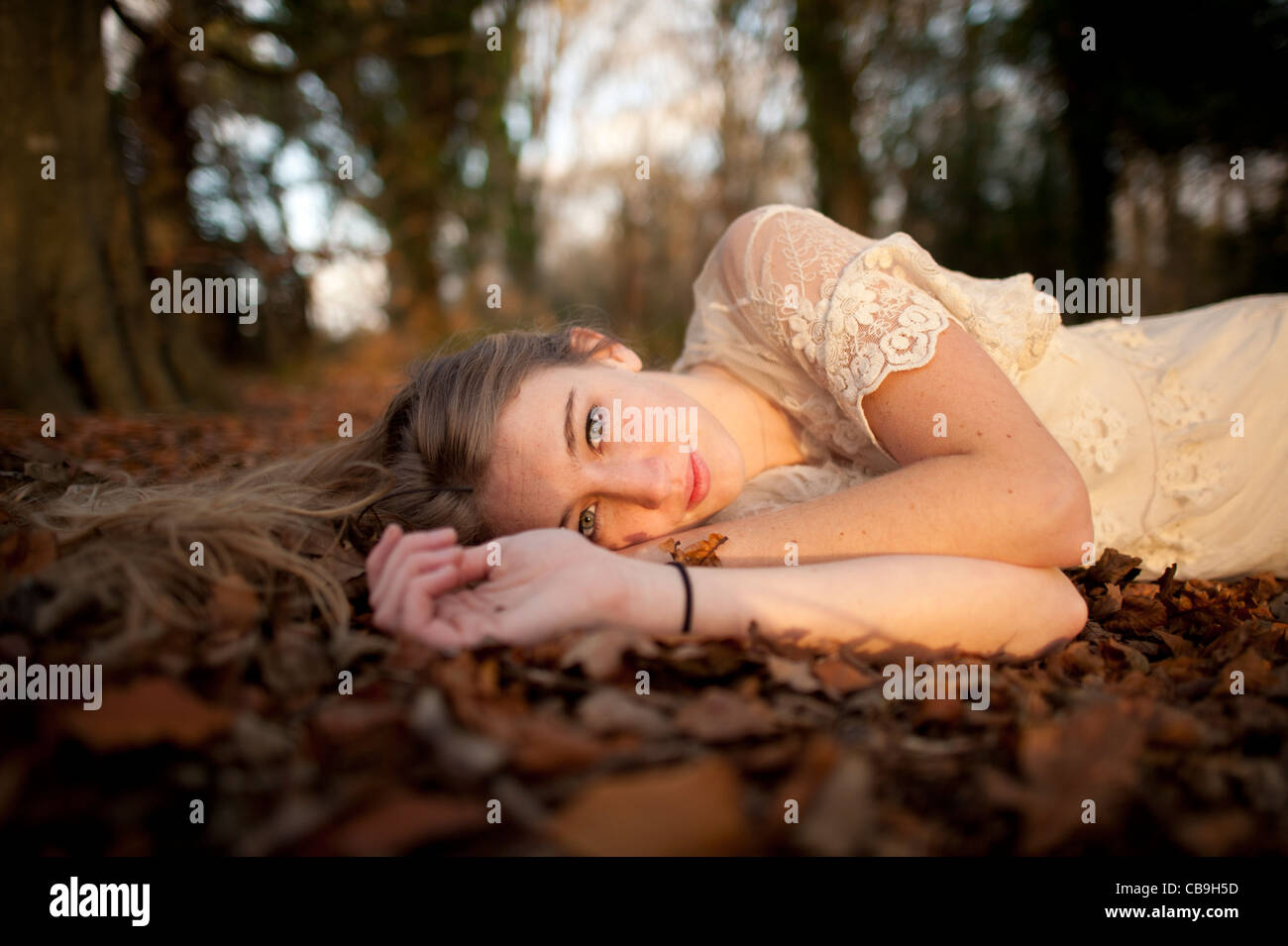 a slim blonde woman girl alone lying down on the ground in woodland autumn afternoon daytime UK Stock Photo