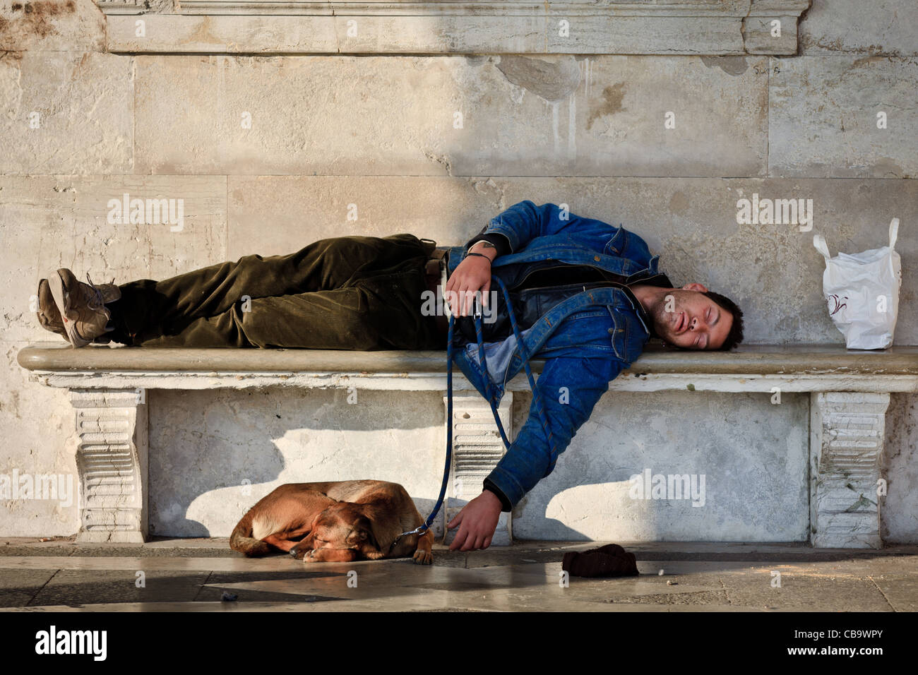 Homeless man with his dog asleep on a bench in Venice, Italy Stock Photo