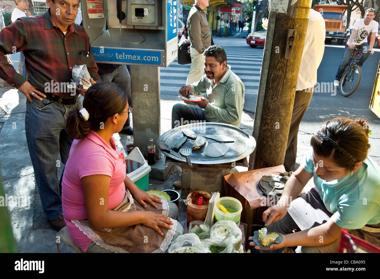 two women preparing blue corn tacos surrounded by happy customers eating on busy street corner Roma district Mexico City Stock Photo