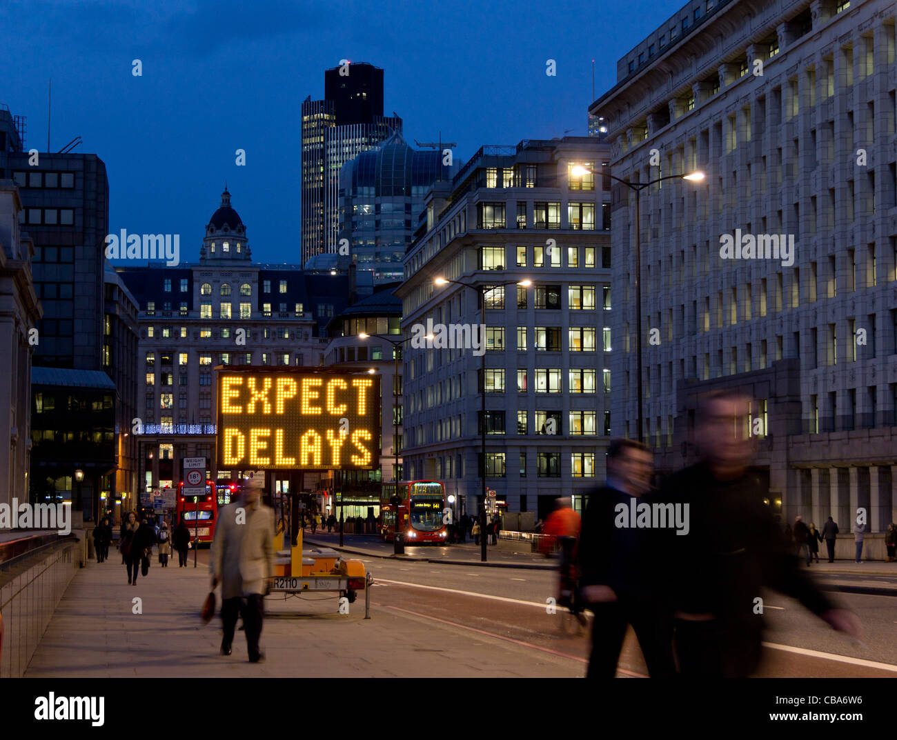 View along King William Street from London Bridge of workers walking home at nightfall; Expect delays electronic roadsign Stock Photo