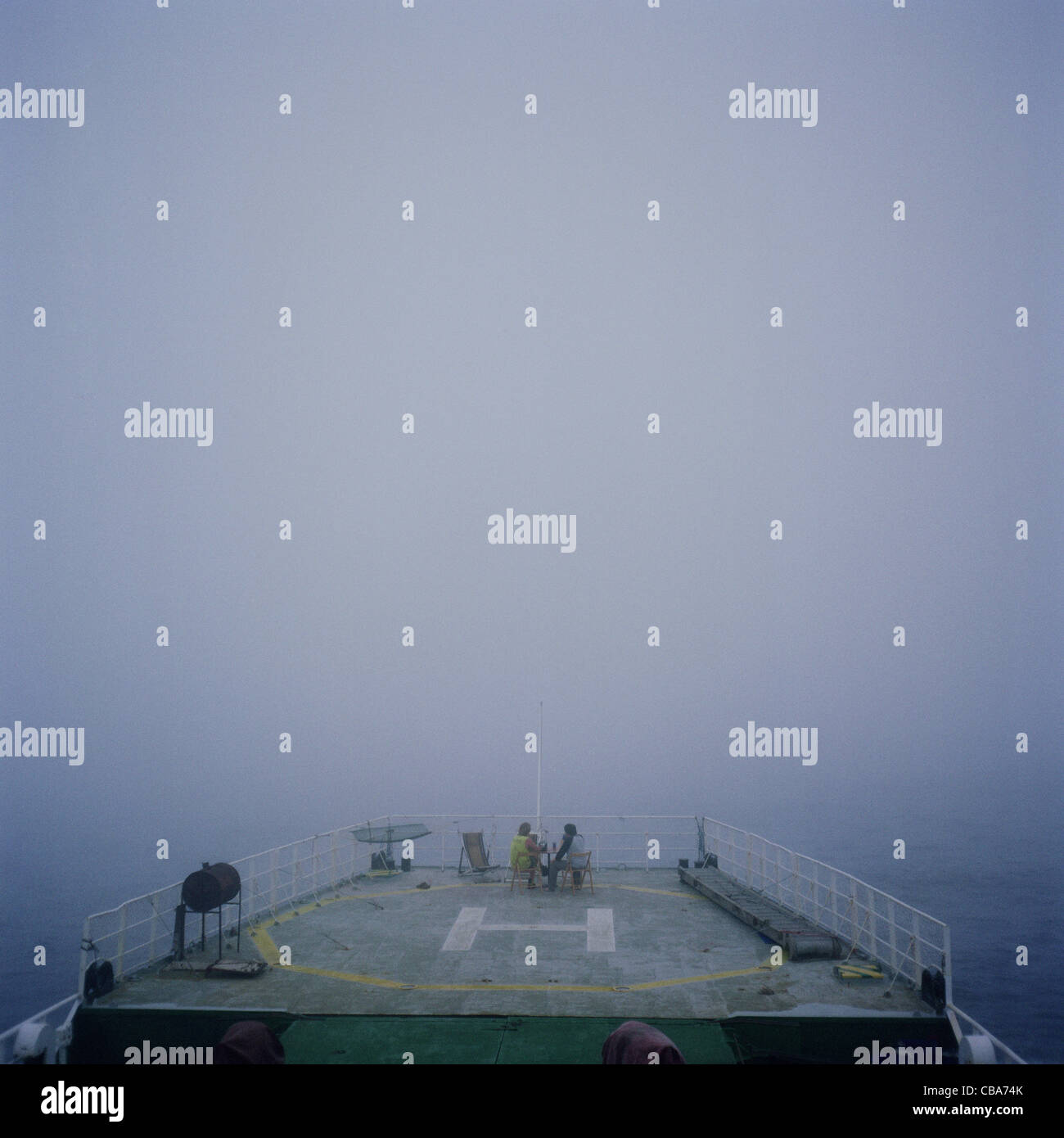 Crew sitting on the helicopter landing pad deck of a ship, in the fog, at sea. Stock Photo