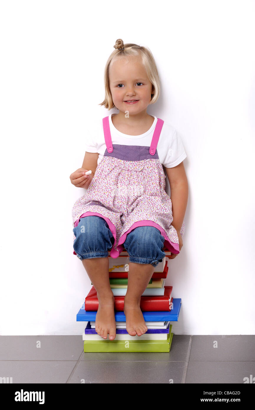 little girl sitting on a stack of books against a wall Stock Photo - Alamy