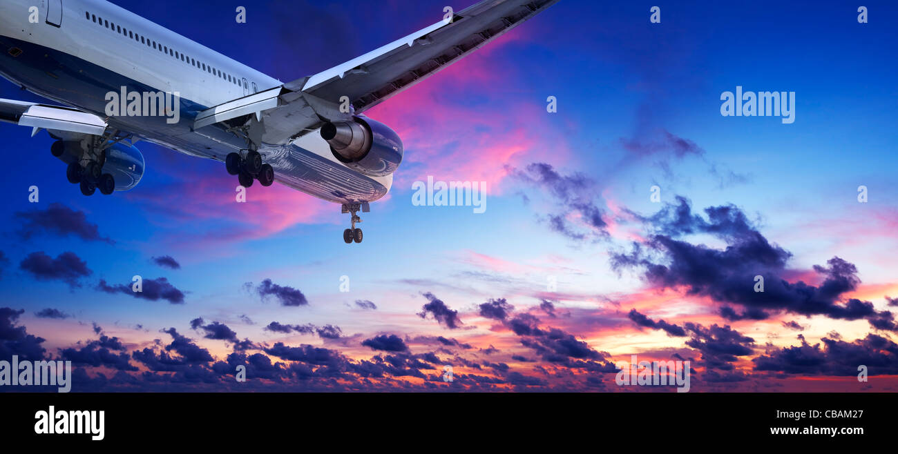 Jet aircraft is maneuvering for landing in a sunset sky. Panoramic composition. Stock Photo