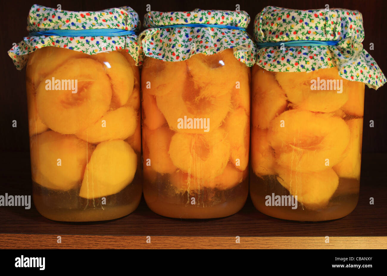 three jars of home canned peaches on a shelf Stock Photo