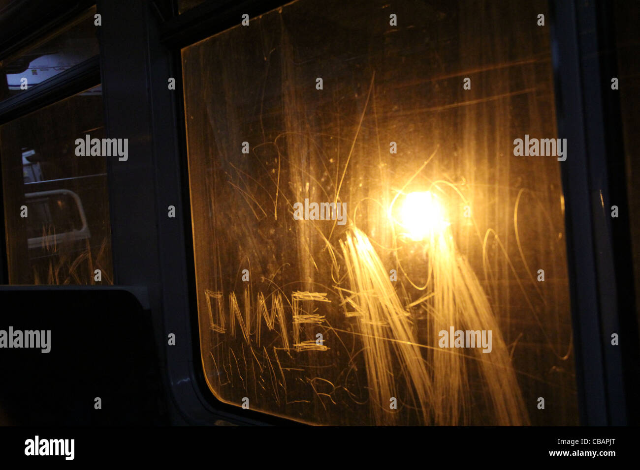 View from inside tube carriage looking towards a light which illuminates graffiti on the train window. Vandalism etching 'on me' Stock Photo