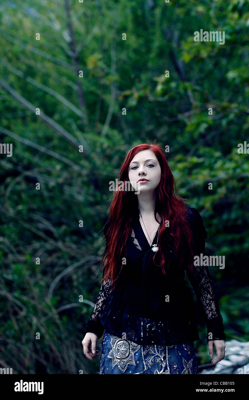 A girl with red hair alone in the forest with trees behind her Stock ...