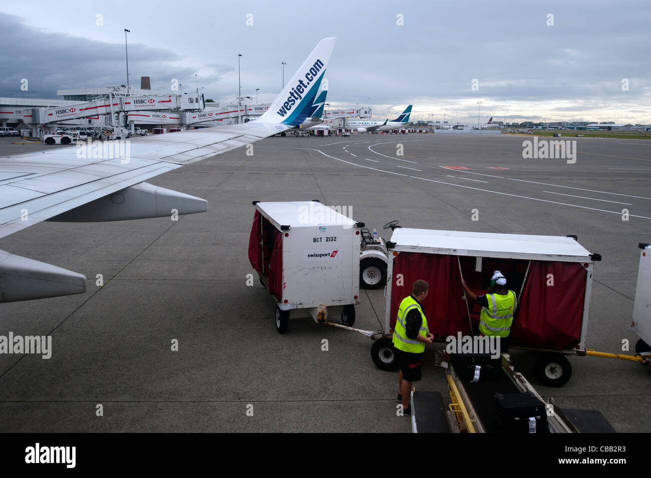 Baggage handlers outside on the tarmac unloading an airplane at an airport Stock Photo