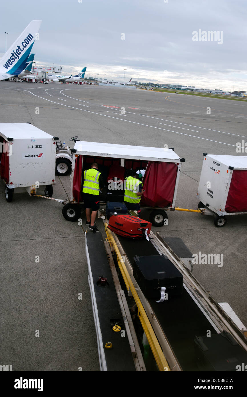 Baggage handlers removing luggage from airplane at airport, Canada Stock Photo