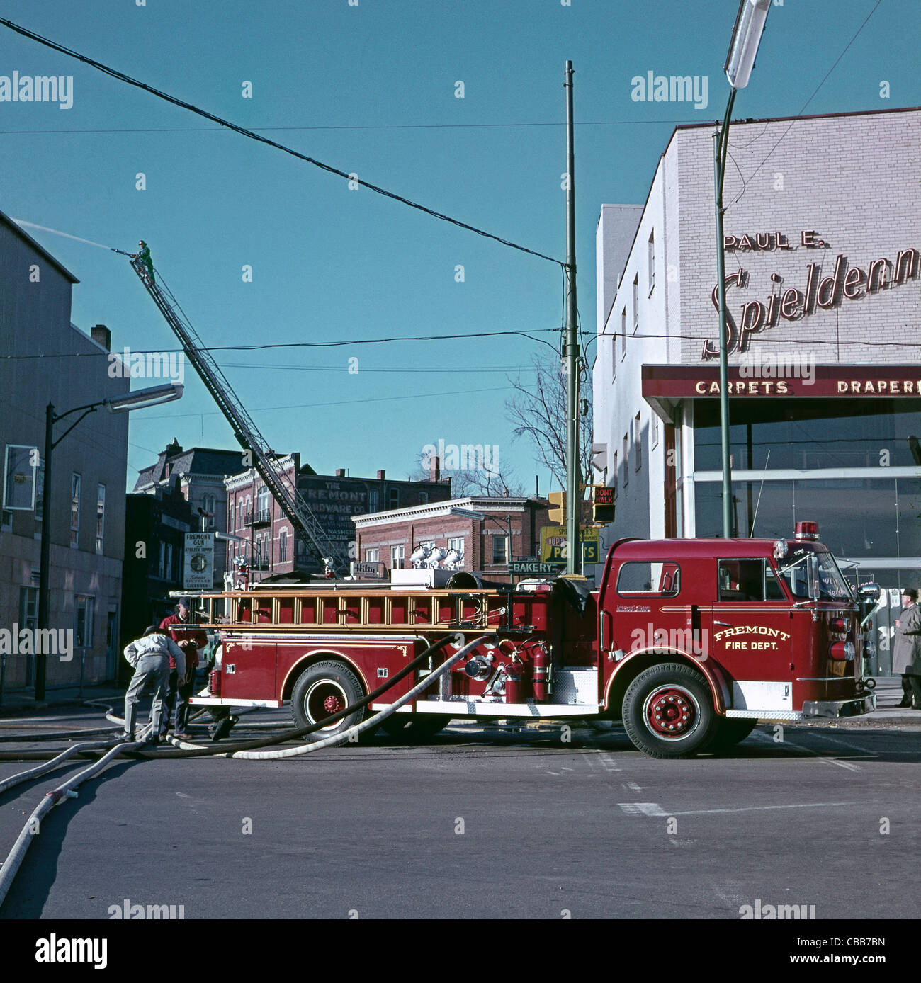 Fire dept trucks attend a fire in Fremont, California, USA c. 1960. The vehicle is pumping water and behind is a fire-fighter on a mechanical ladder Stock Photo