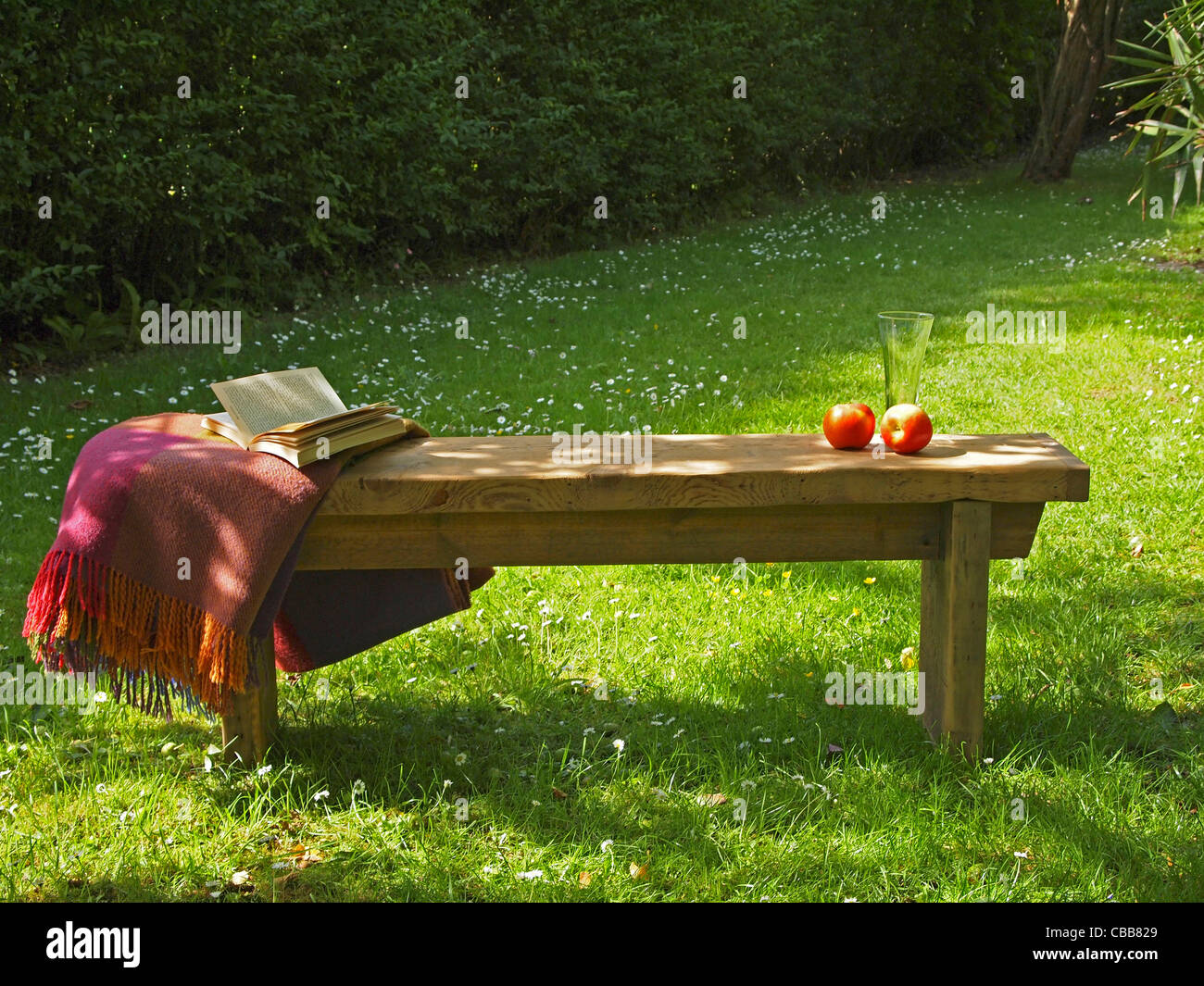 A relaxed atmosphere in a sunny English country garden - the wooden bench has a book, blanket and refreshments on it Stock Photo