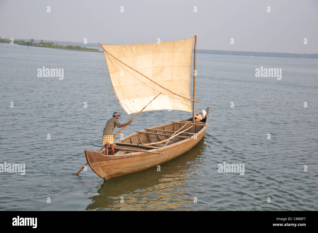 a man rowing a sailboat using a stick in backwaters of kerala, alapuzha
