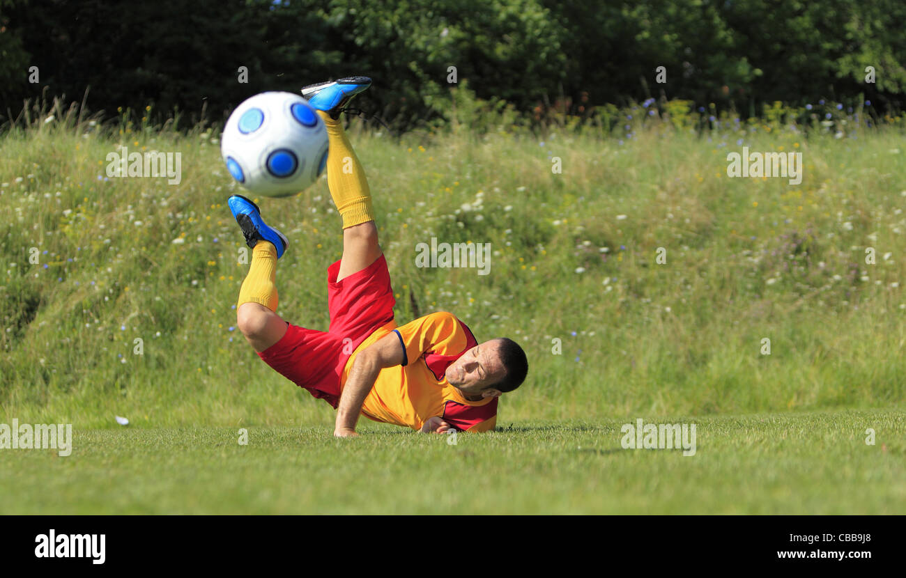 A soccer player on the ground after he kicked the ball in an acrobatic