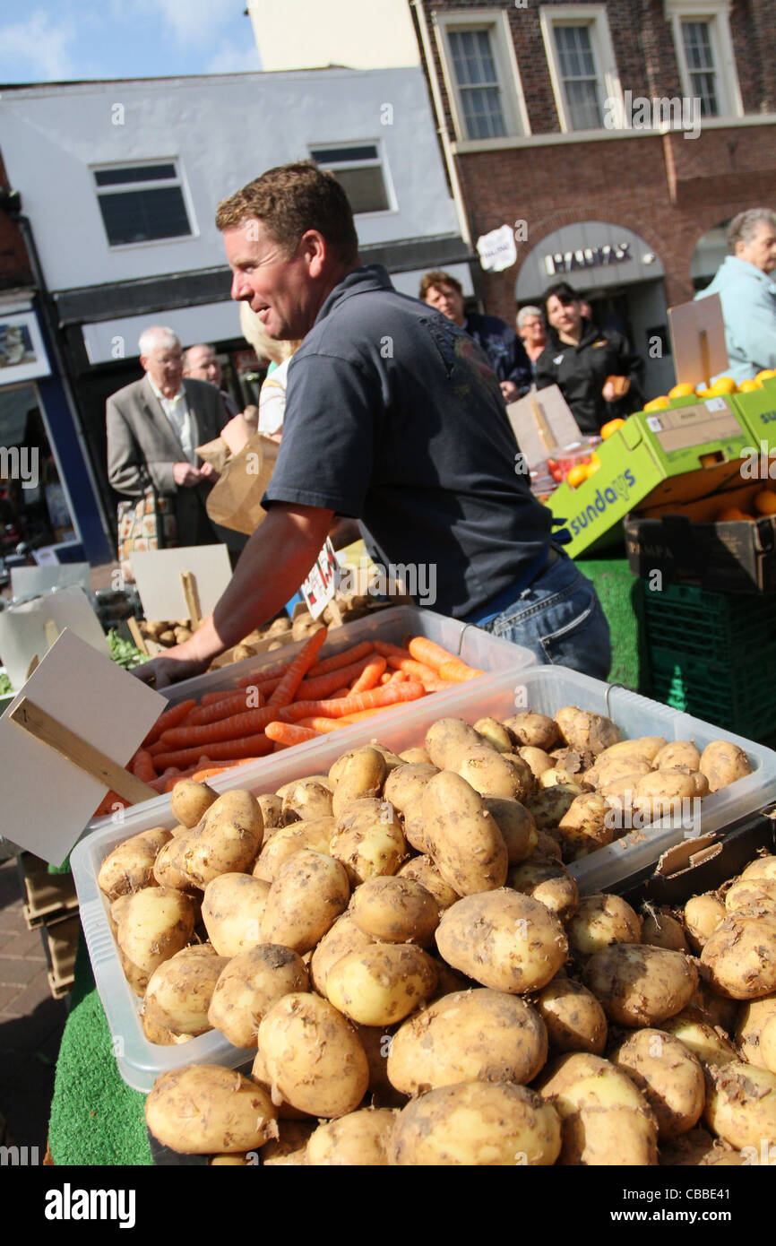 greengrocer on Doncaster Market in sunshine with new potatoes in foreground Stock Photo