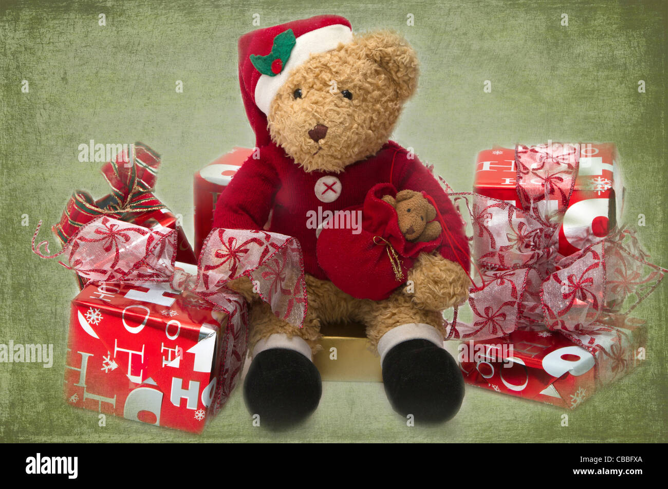 Teddy at Christmas. Well loved child's teddy dressed as Santa sitting among presents. Stock Photo