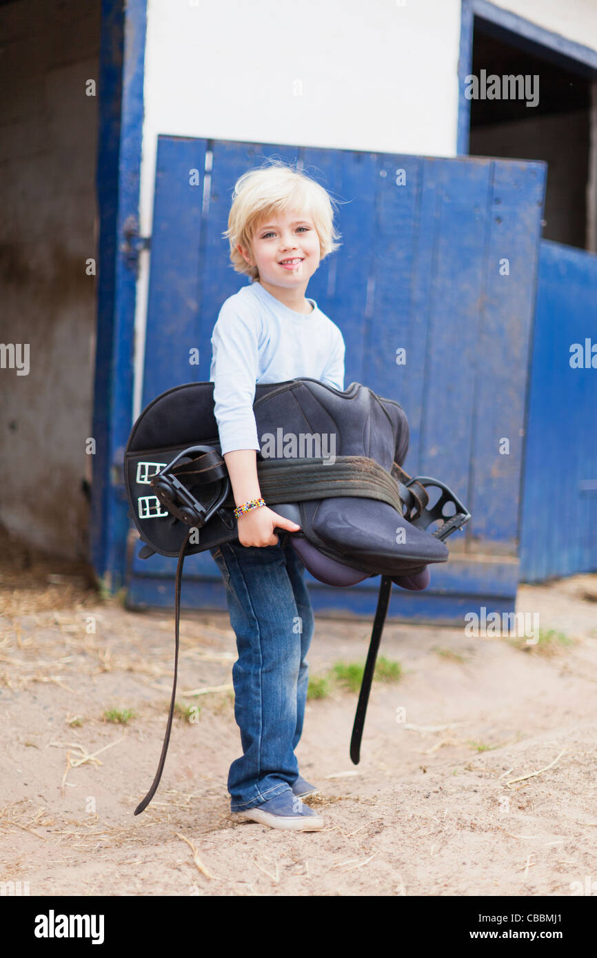 Boy carrying horse saddle Stock Photo