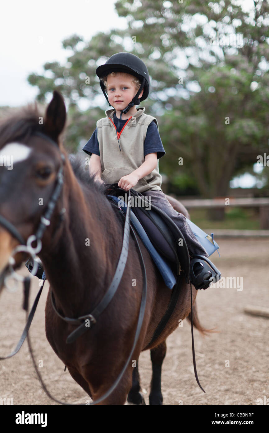 Boy riding horse in yard Stock Photo