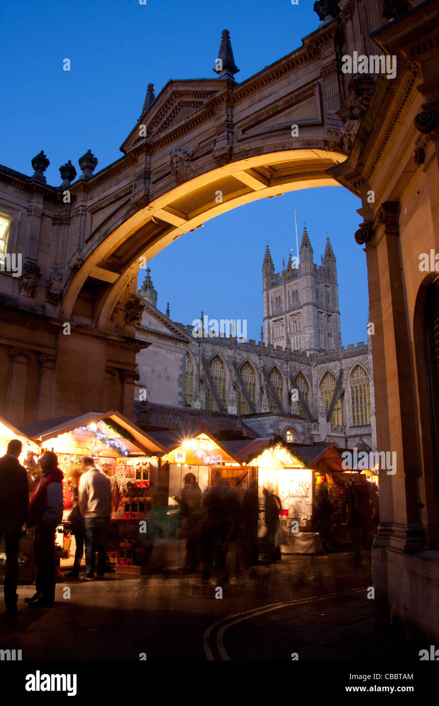 Bath Abbey framed by arch with Christmas market stalls and people underneath Bath Somerset England UK Stock Photo
