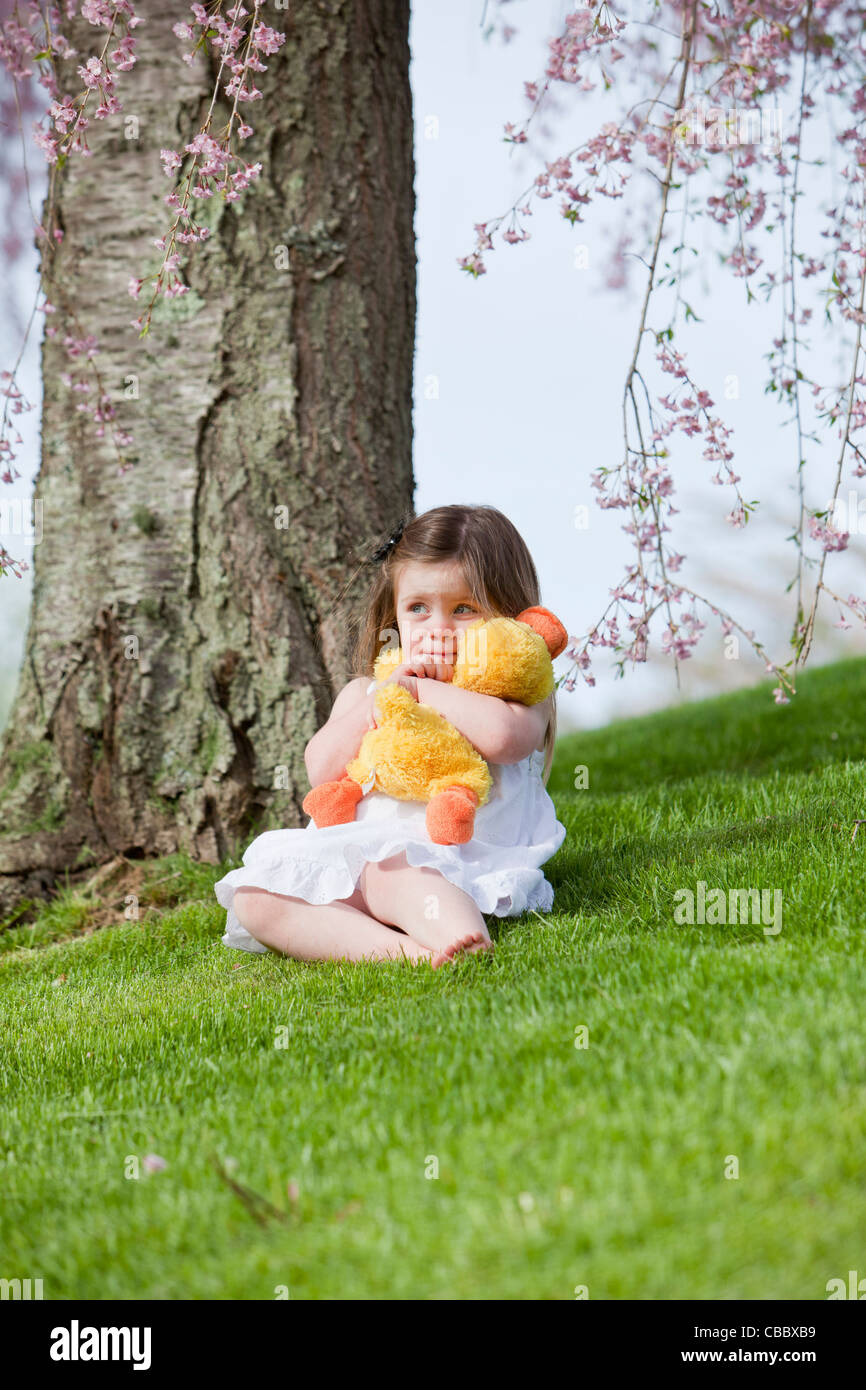 Sad little girl with her toy sitting under a tree Stock Photo - Alamy