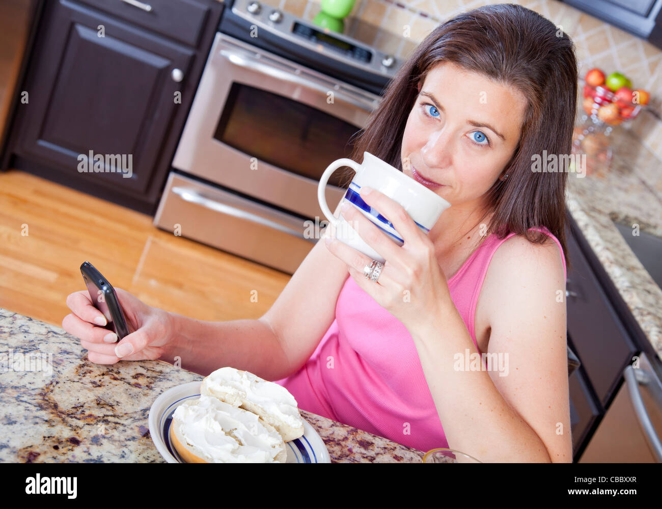 Pretty woman eating a bagel for breakfast in the kitchen Stock Photo