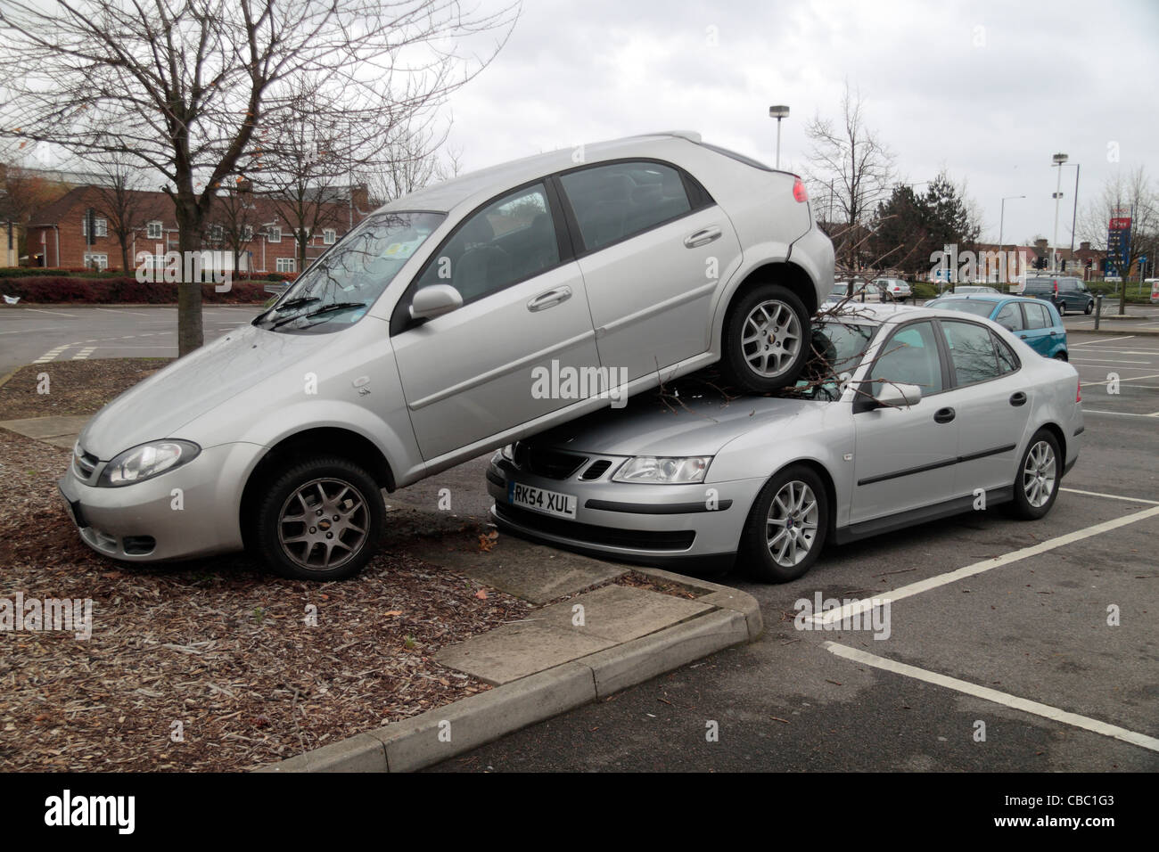 A car park incident where one car was accidentally reversed up a kerb, into a tree and up onto the bonnet of another car. Stock Photo