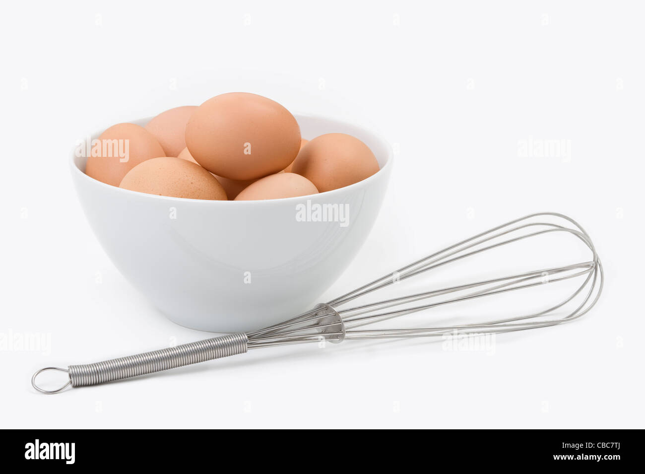 brown hens eggs in a white bowl with a stainless steel whisk against a white background Stock Photo