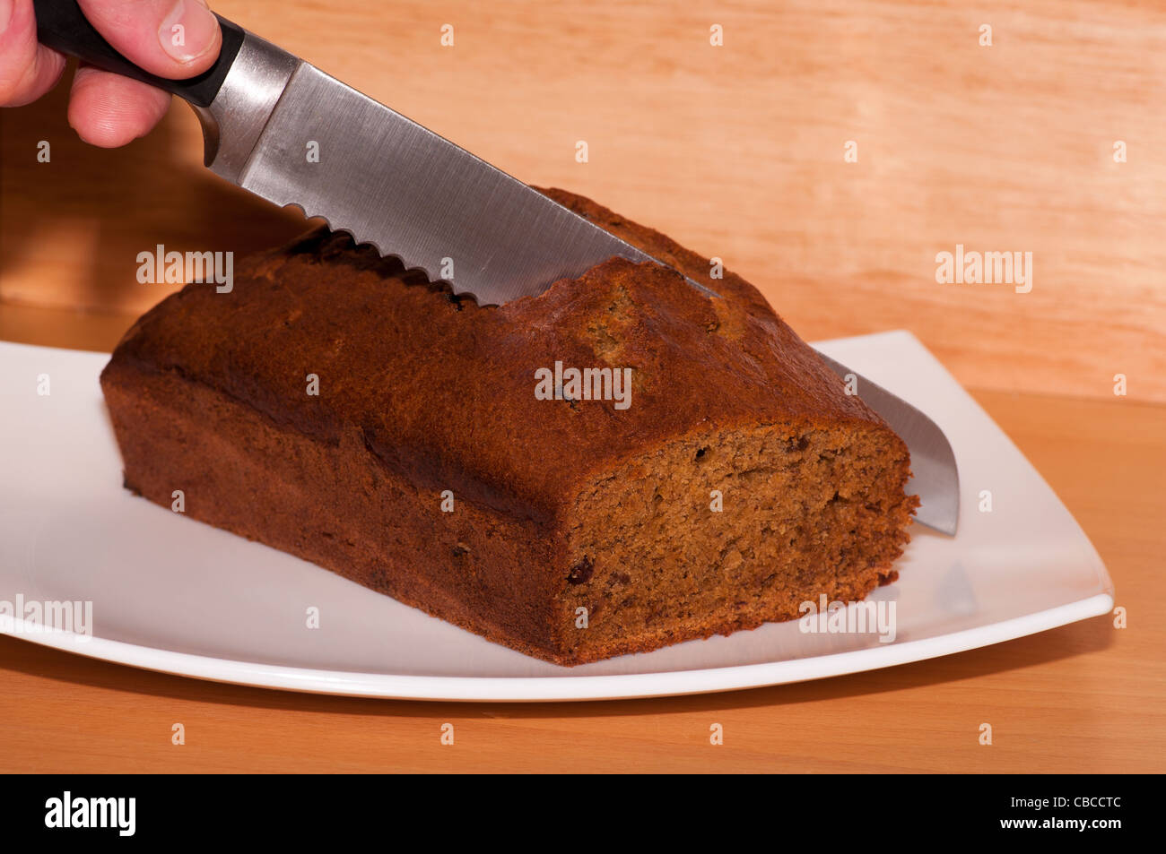 Hand Holding A Knife Cutting A Slice Of Fresh Home Made Baked Cooked Banana Cake On A White Plate Home Baking Stock Photo