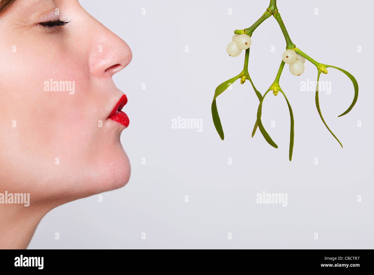 Photo of a woman with her eyes closed and red lipstick on waiting to be kissed under the mistletoe. Stock Photo
